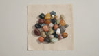 A pile of mixed tumbled gemstones in greens, reds and creams on cotton-rag paper video