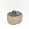 Small river stone pot with stone lid on a clean white surface against a white wall