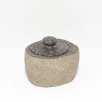 Small river stone pot with stone lid on a clean white surface against a white wall