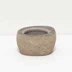 Small river stone pot with stone lid on a clean white surface against a white wall