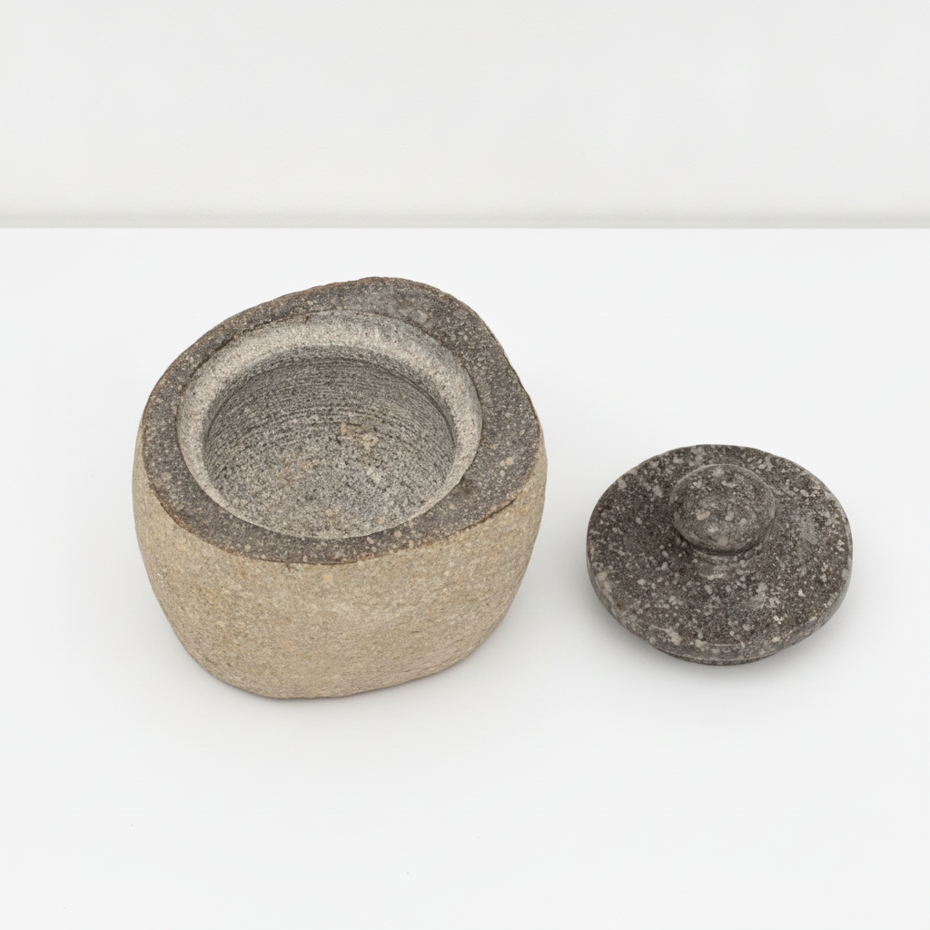 Small river stone pot with stone lid on a clean white surface against a white wall