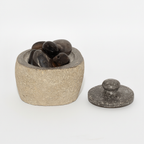 Small river stone pot with stone lid on a clean white surface against a white wall