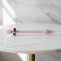 Rose quartz shiva lingam wand on a marble table with a marble wall behind