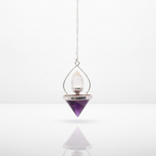 Amethyst and rock quartz lantern of life pendulum on a clean white surface against a white wall