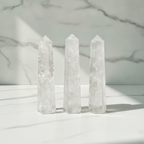 Clear quartz six face obelisk points on a marble table with a marble wall behind