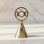 Triple moon brass altar bell on a marble table with a marble wall behind