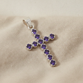 Silver-plated crucifix pendant set with deep purple stones, on linen