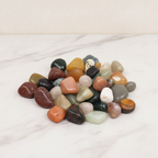 A pile of mixed tumbled gemstones in greens, reds and creams on cotton-rag paper - view 2