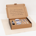 Kraft self-care kit box open flat, showing scrub tins, serum bottle and bath salt tubes