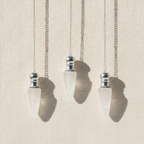 Three clear quartz pendulums with silver caps hanging from fine chains