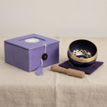 Brass and black singing bowl with striker, purple cushion and lilac box