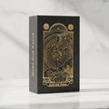 Gold foil tarot card set in its black and gold foil gift box, standing on a white marble table