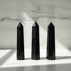 Black tourmaline six face obelisk on a marble table with a marble wall behind
