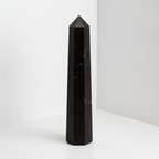 Black tourmaline six face obelisk standing upright, polished faces catching the light