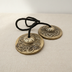 A pair of brass tingsha cymbals joined by a black cord, on cotton canvas - view 3