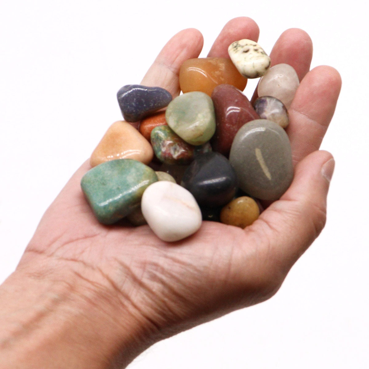 A pile of mixed tumbled gemstones in greens, reds and creams on cotton-rag paper - view 6