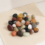 A pile of mixed tumbled gemstones in greens, reds and creams on cotton-rag paper - view 10