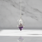 Amethyst dowsing pendulum hanging above a marble table